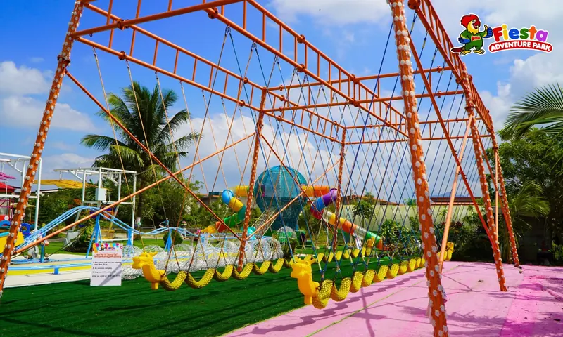 A long yellow dragon swing hanging from an orange steel frame, with the rainbow tube slide tower behind it