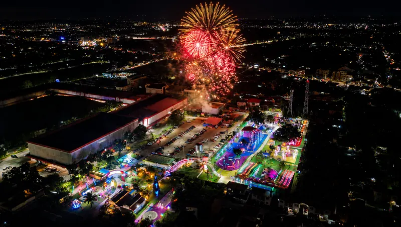 Fireworks exploding high above the lit-up park at night, seen from a drone