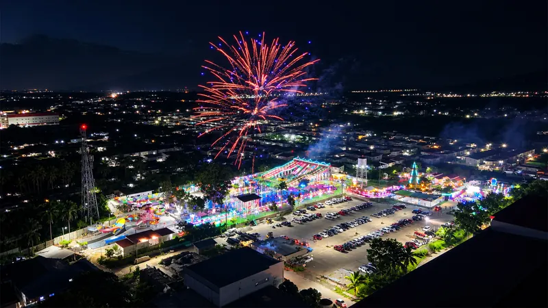 Aerial view of red fireworks bursting above the brightly lit park and car park at night