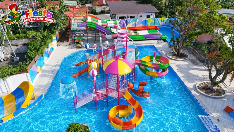 Shallow kids pool with a small multi-slide play structure, mushroom fountains and floating rings