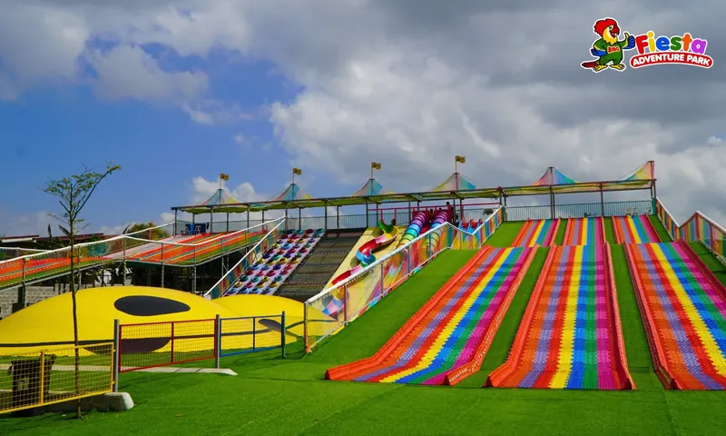 Wide view of the rainbow slide hill with striped lanes running down to a green lawn