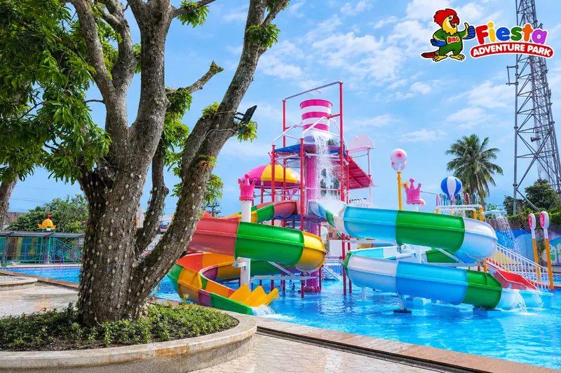 A splash play tower with slides and a tipping bucket beside a tree