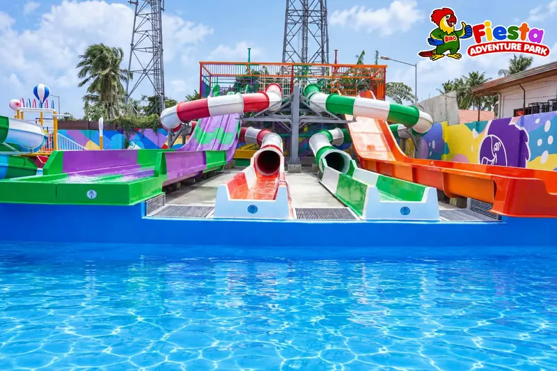 Four brightly coloured water slides in red, green, purple and orange running side by side into a clear blue pool