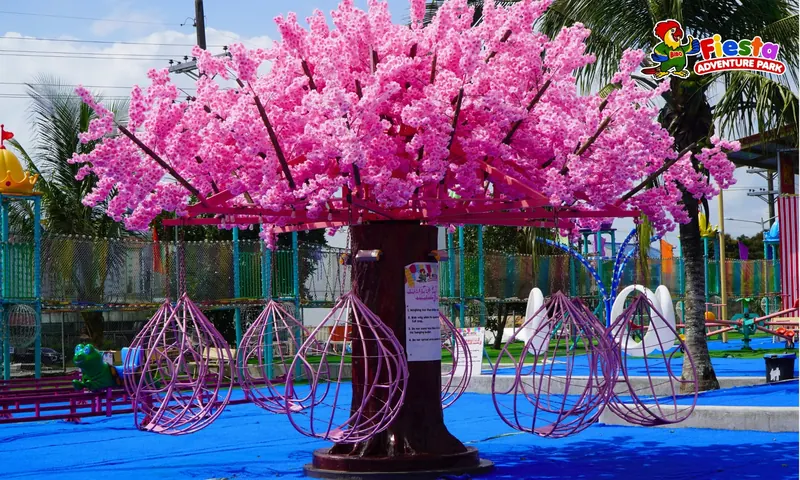 Hanging teardrop seats under a bright pink cherry blossom canopy ride on a blue play surface